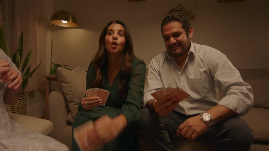 Group of happy friends smile and laugh while playing cards at home