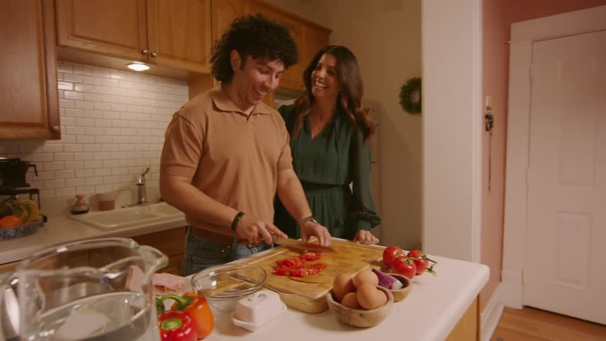 Young man and woman talk in kitchen as he cuts tomatoes