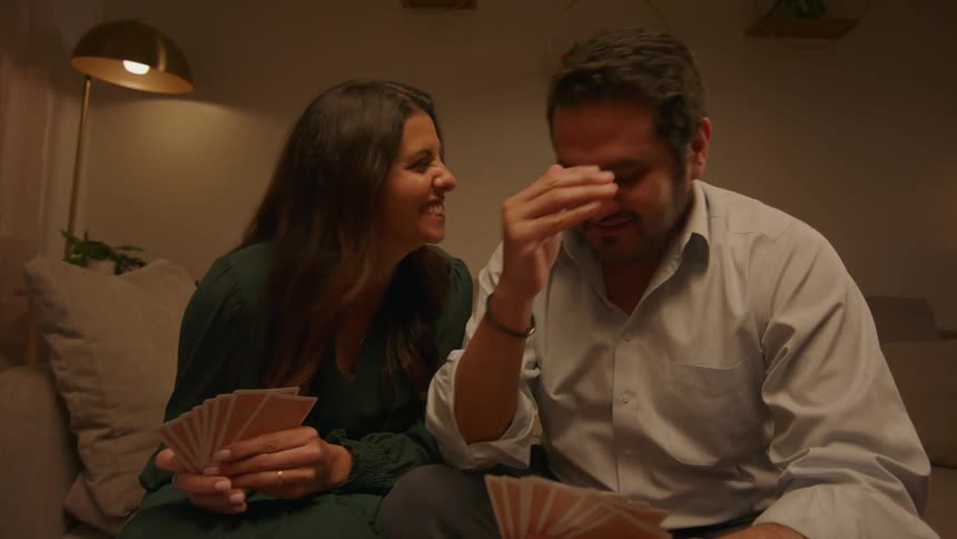 Men and women playing card games while seated on the couch indoor at night