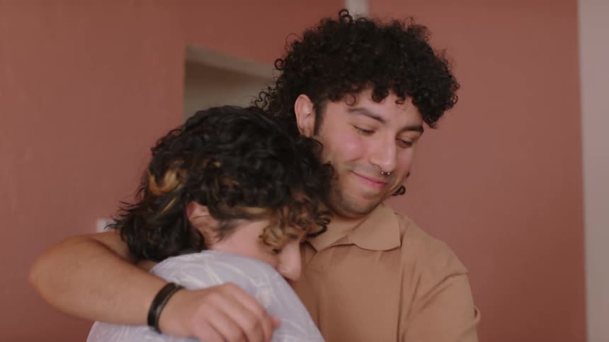Man hugs a lady while patting her back in a room during the day