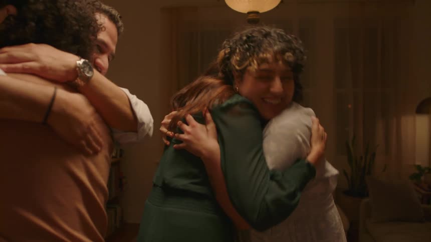 Two men and two women smiling while hugging each other in the living room at night