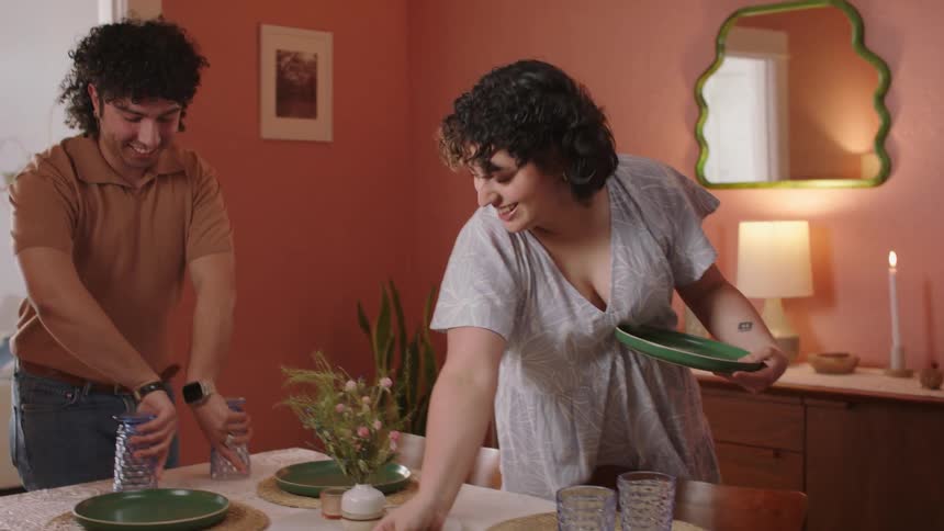 Man and woman playfully set plates on the dinner table