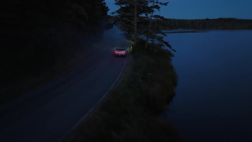 A car was driving along a road near a lake at dusk