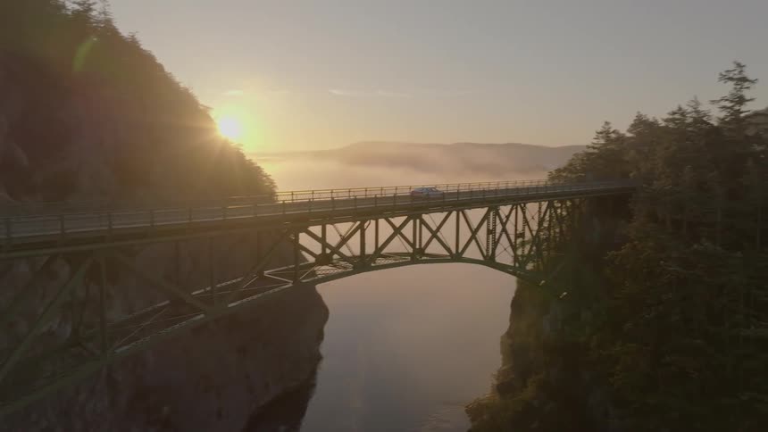 A car driving on a bridge over a gorge at sunset