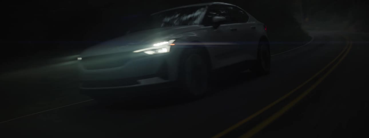 Sleek sedan with bright white headlights driving on a curved highway through the woods after sundown