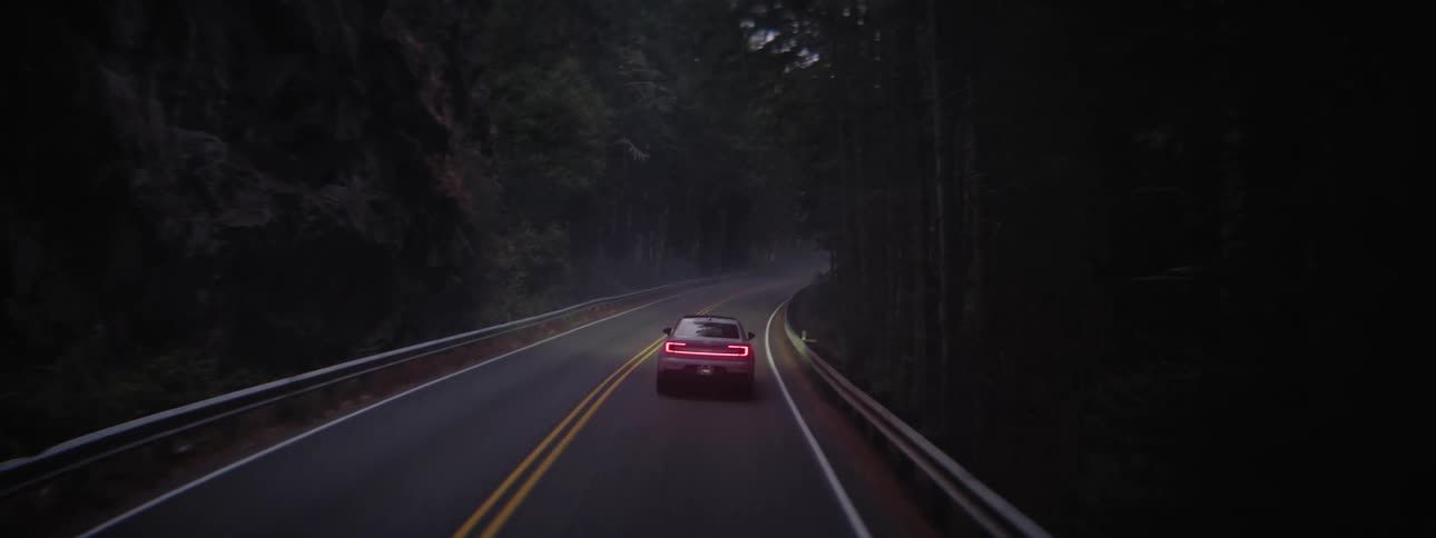 Rear view of a Polestar EV driving down a highway through fog surrounded by dense woods with red tail lights illuminated