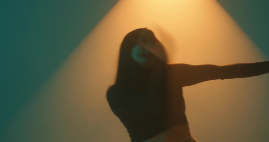 A woman doing dance moves on a blue background with a yellow light