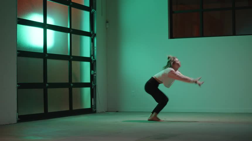 Woman dancing an energetic choreography alone in a room backlit by green light