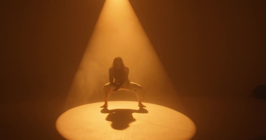 A woman performance an artful modern dance beneath a bright spotlight