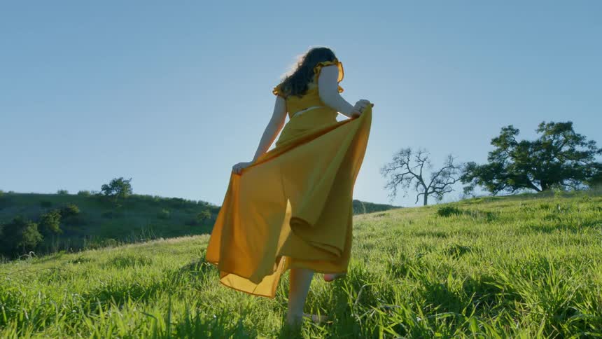 Woman in a yellow dress climbing a hill on a cloudless blue sky day