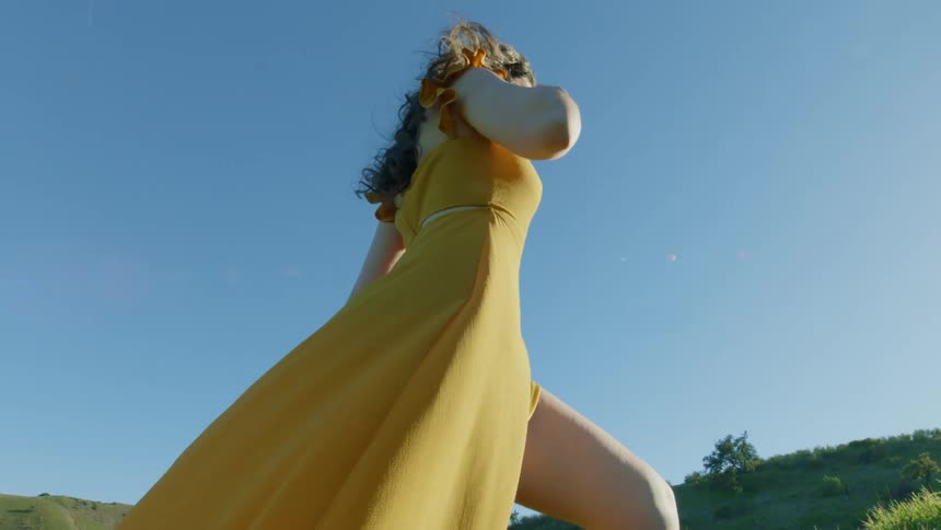 A woman walking on a hill in a long yellow dress