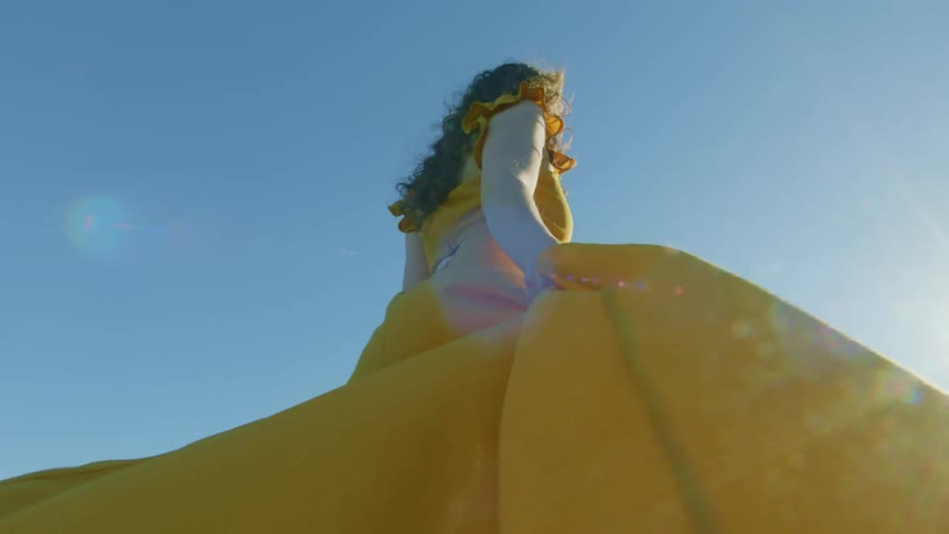 Woman with curly hair and a yellow dress walks up green hill