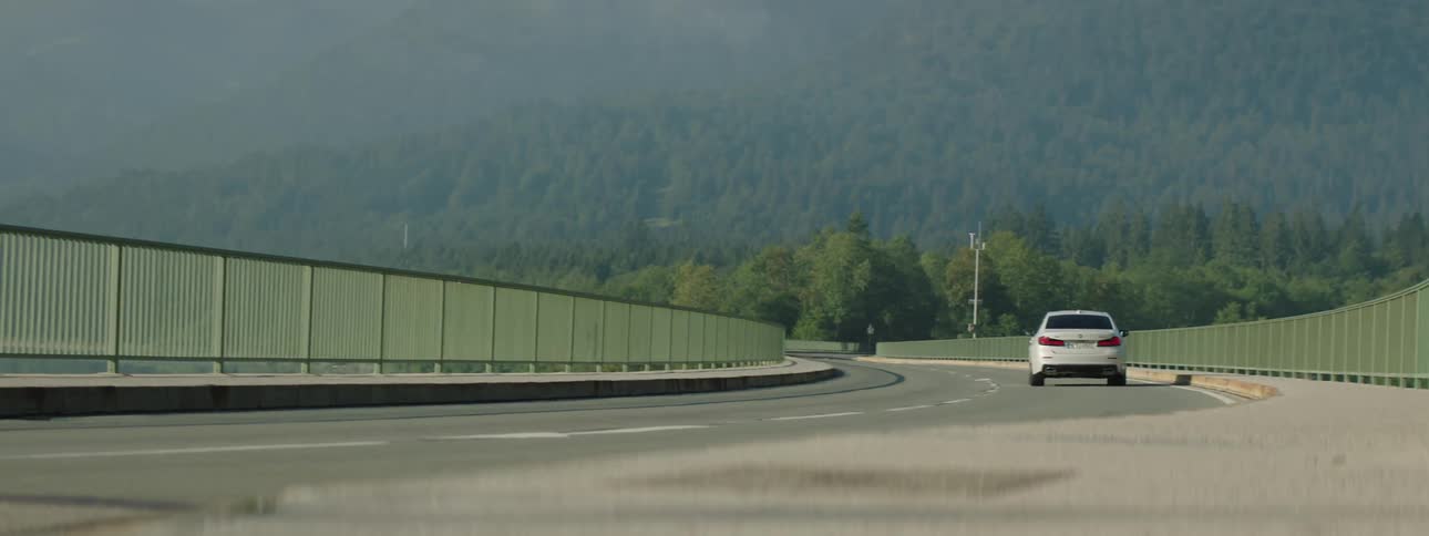 Sedan car passing on a road next to a mountain with forest