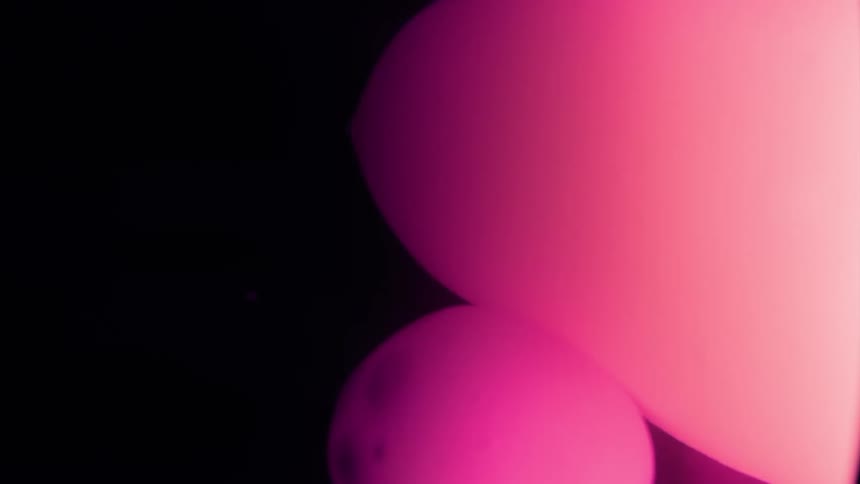 A closeup of pink and purple glowing orbs merging against a dark background