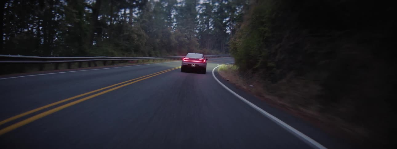 A Polestar Electric Vehicle travels on a road around a forested mountain