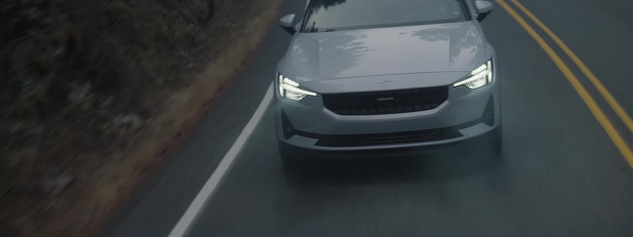 A Polestar electric vehicle travels around a curve with headlights on