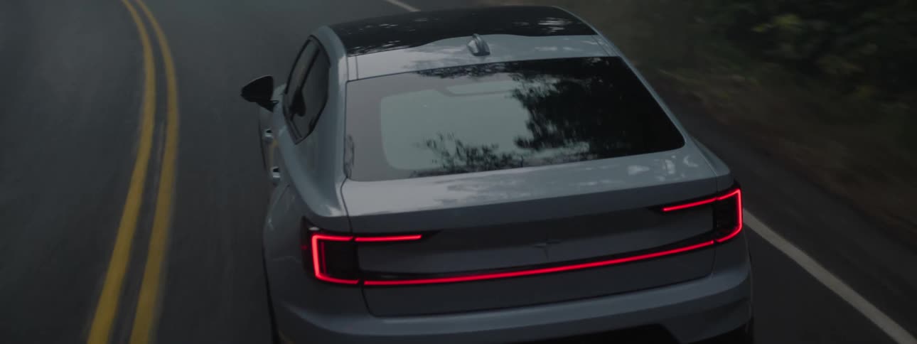 A white Polestar electric vehicle with sunroof driving on a curvy road through fog surrounded by forest