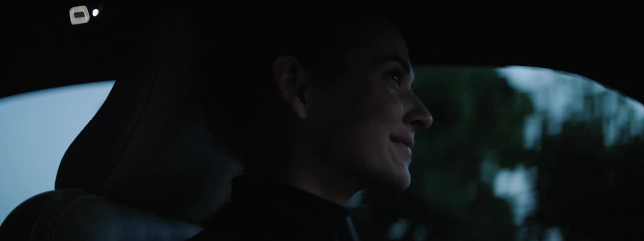 A woman smiles as she drives along a street in her vehicle at dawn