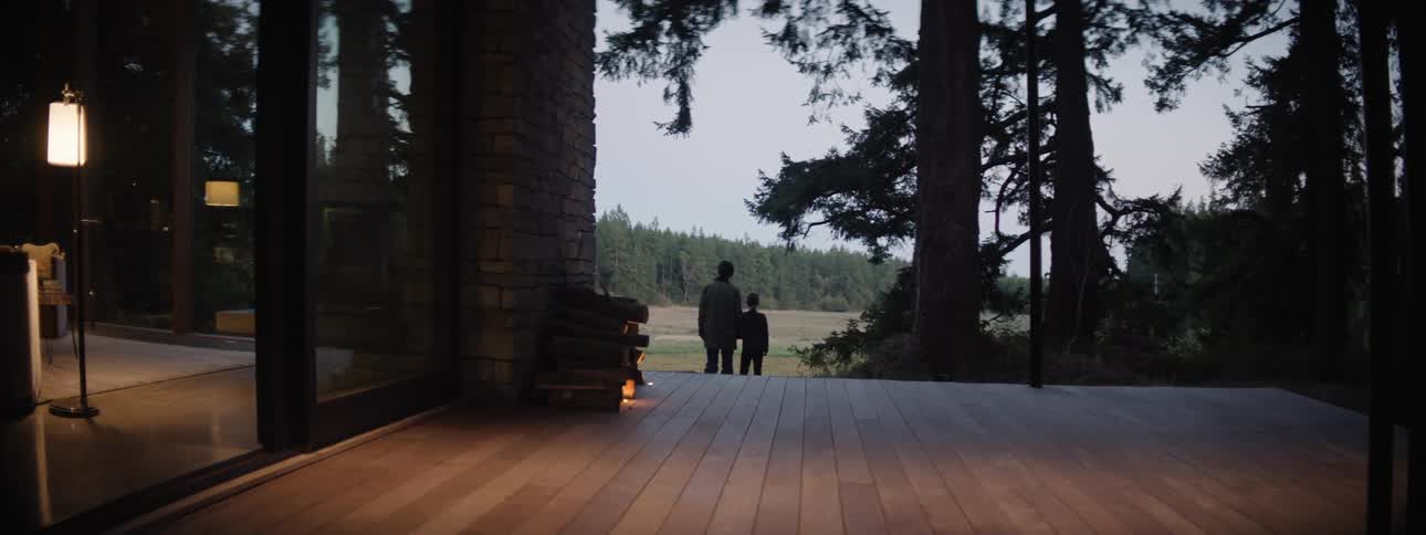Silhouette of a mother and daughter walking next to a modern home and deck surrounded by trees