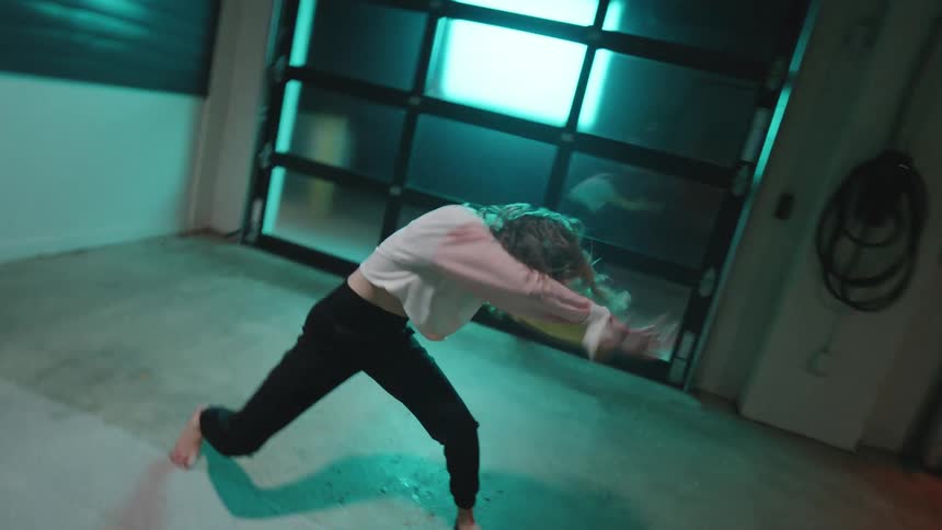 Cheerful young woman dancing artistically in an indoor space backlit by colorful lights