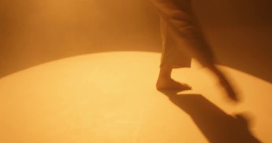 A woman with dark hair energetically dances under a bright spotlight