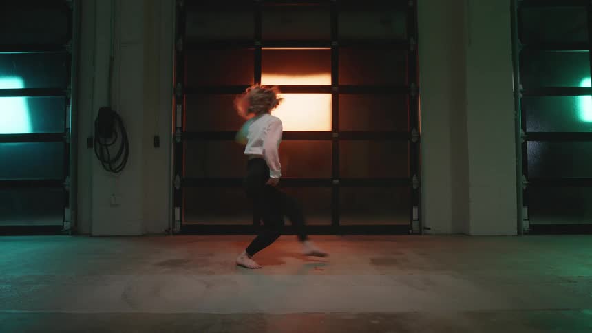 A young woman performs a modern dance in large room backlit with colorful lights