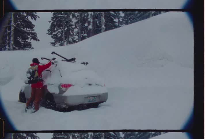 A person is removing snow from his car in a region with a completely snowwhite ground