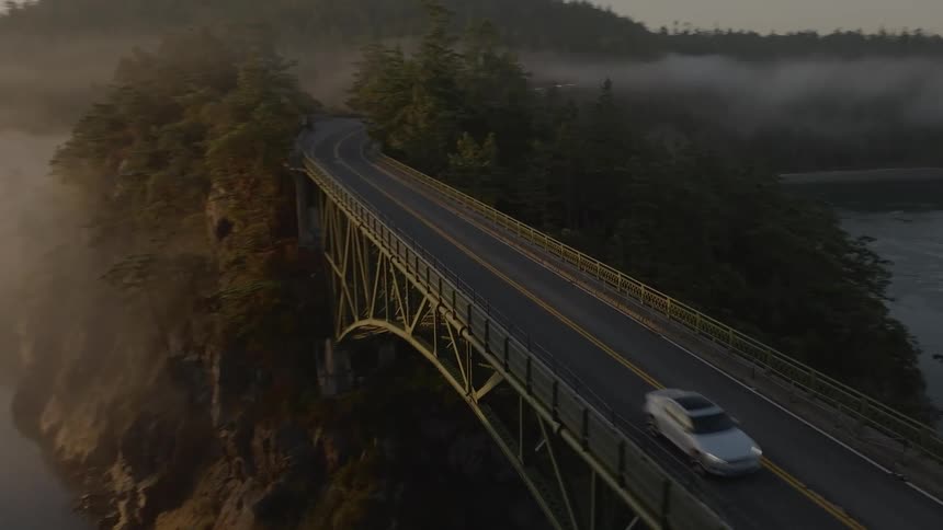White sedan vehicle crossing a suspension bridge on a morning