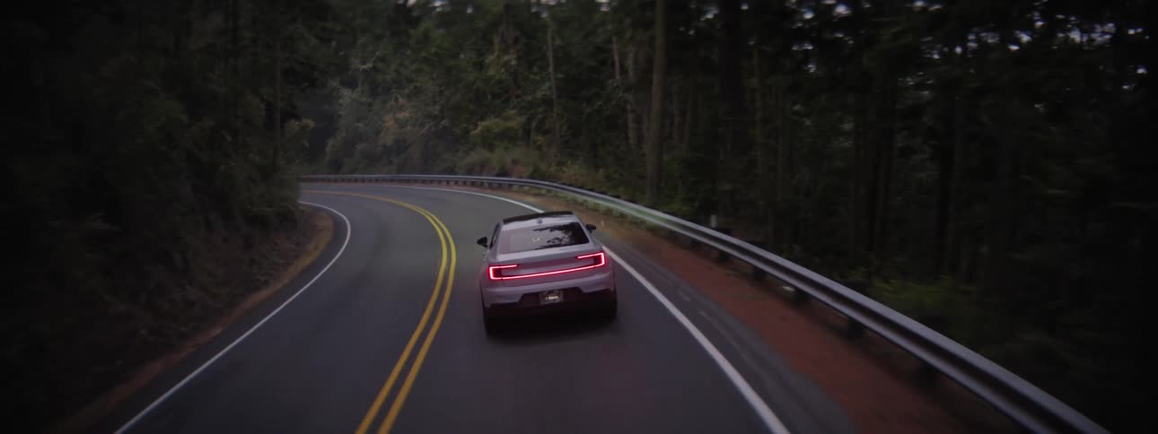 EV Polestar driving on a road through a forest at dawn