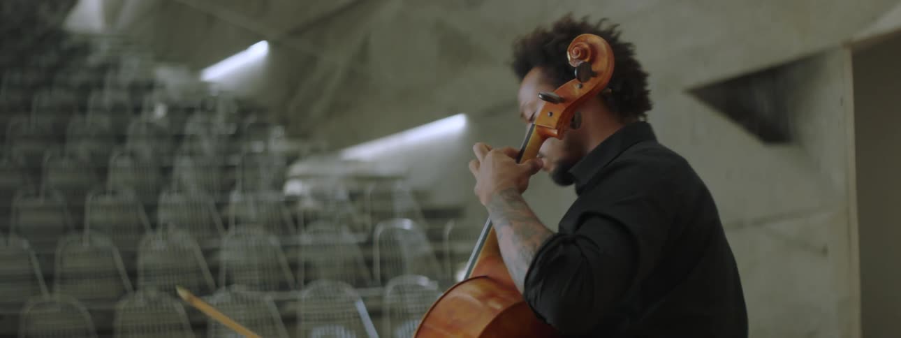 A male cello performer practices on stage in an empty auditorium