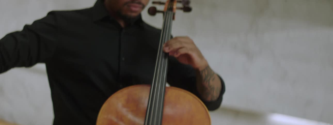 A man playing cello while seated indoor during the day