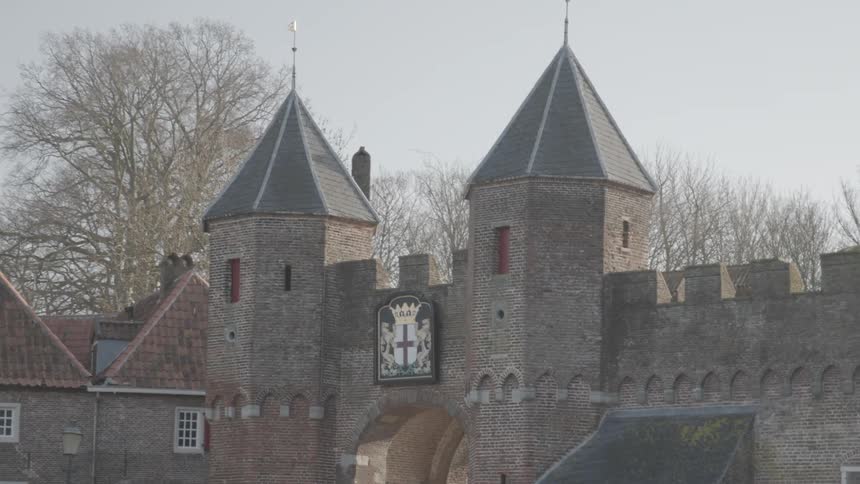 A medieval castle with two round towers with a coat of arms displayed in the stone wall