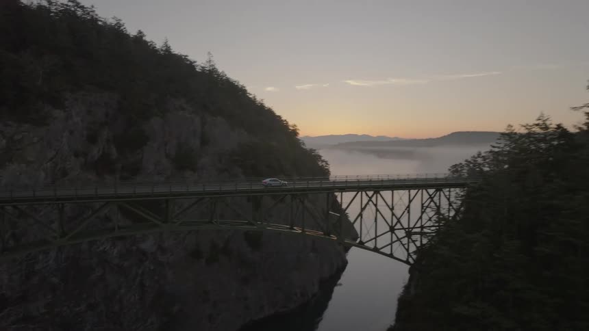 A bridge across a rocky gorge with a car driving on it over a river
