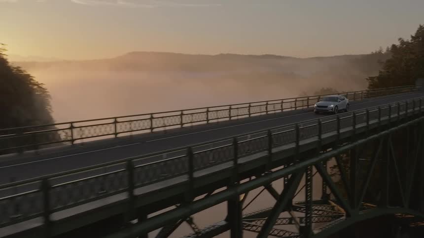 A car driving over a bridge passing beside a mountain