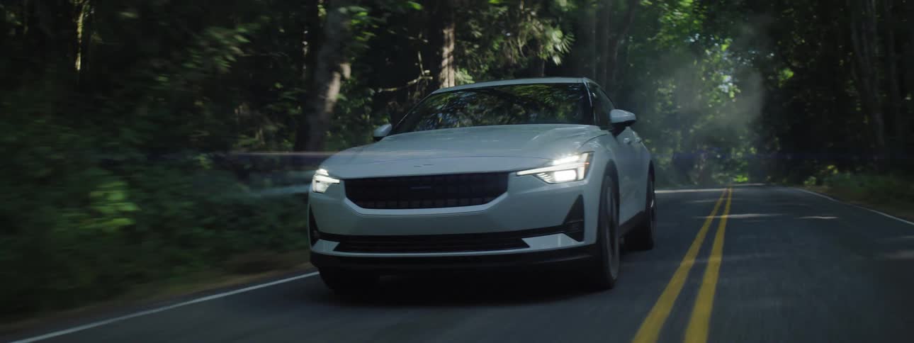 A white automobile Polestar electric vehicle travels on a road through the forest