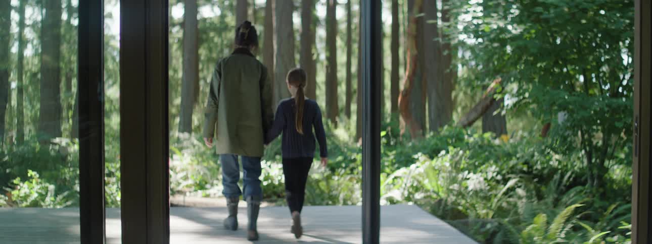 Mother holding her daughters hand and leaving their modern house in the middle of a forest during the day