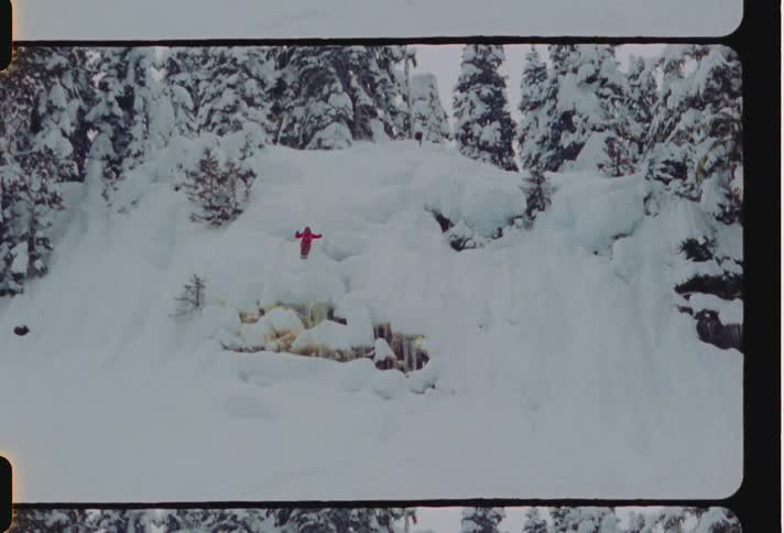 A person in red is jumping off a snowcovered ledge amidst snowy trees