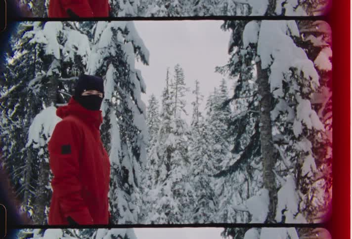 Person wearing ski mask stands among frozen conifers during winter