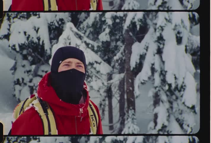 A man wearing a face covering stands outside near snowcovered trees