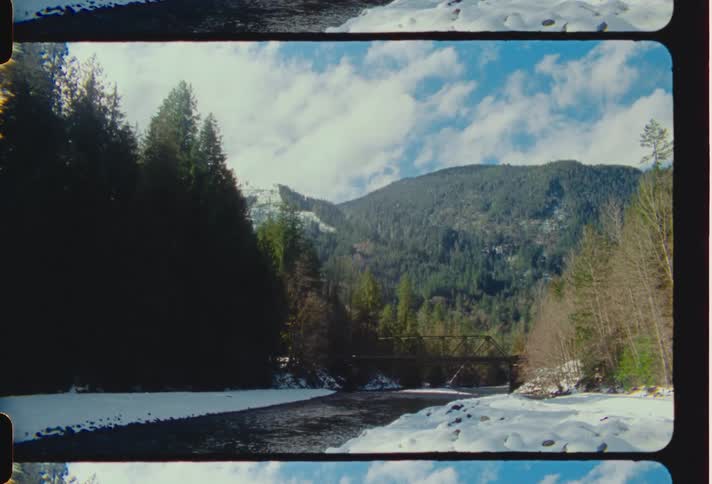 The landscape features a picturesque scene with a bridge spanning over a tranquil river framed by a distant mountain slope