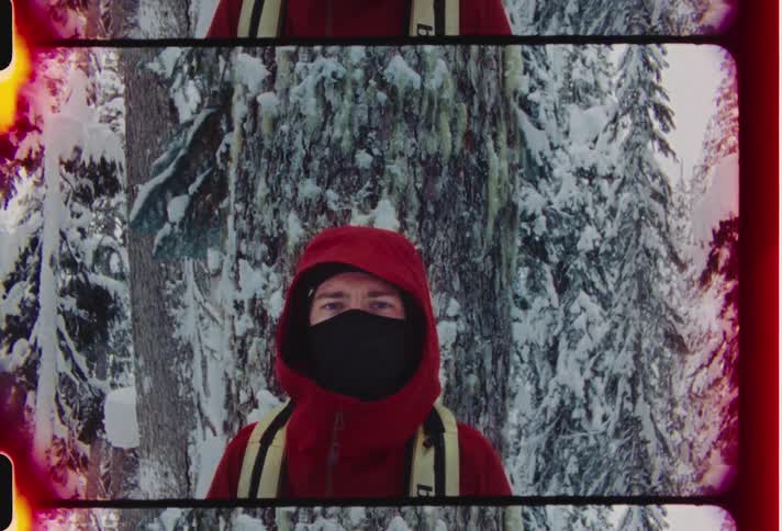 A man in a read jacket poses in a snowy forest with his face partially covered