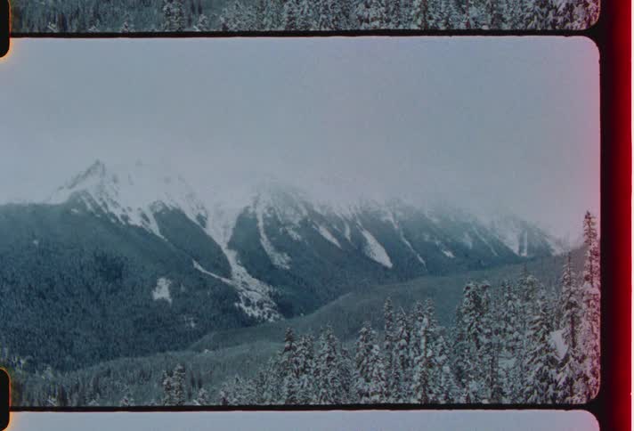 A mountain range covered in snow under the clouds caught on vintage film