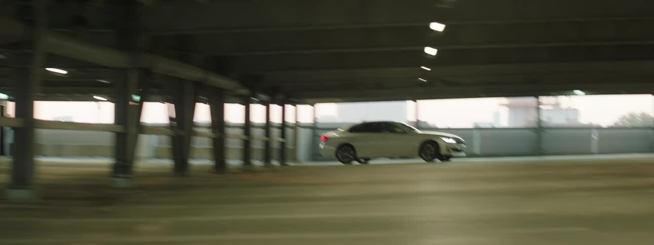 A white car drives in a city parking garage