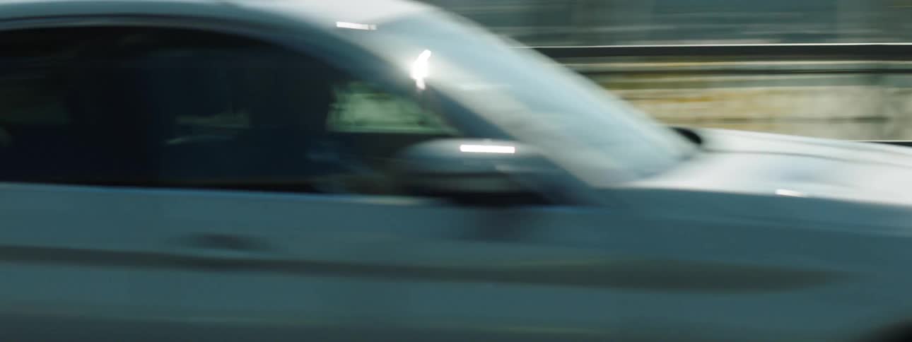 A white car driving on a road behind metal columns