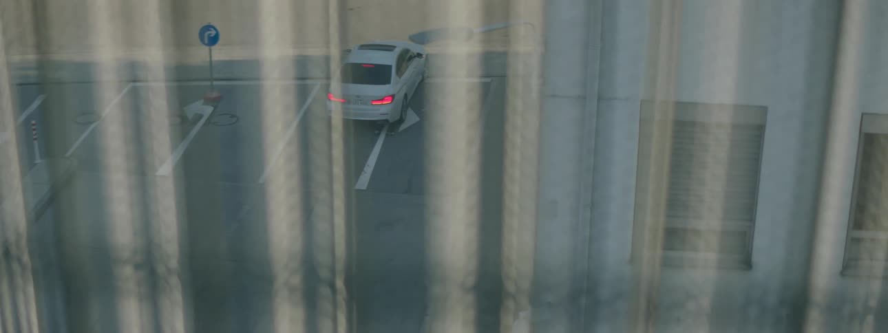 A white car driving on the city street seen from the window of an apartment