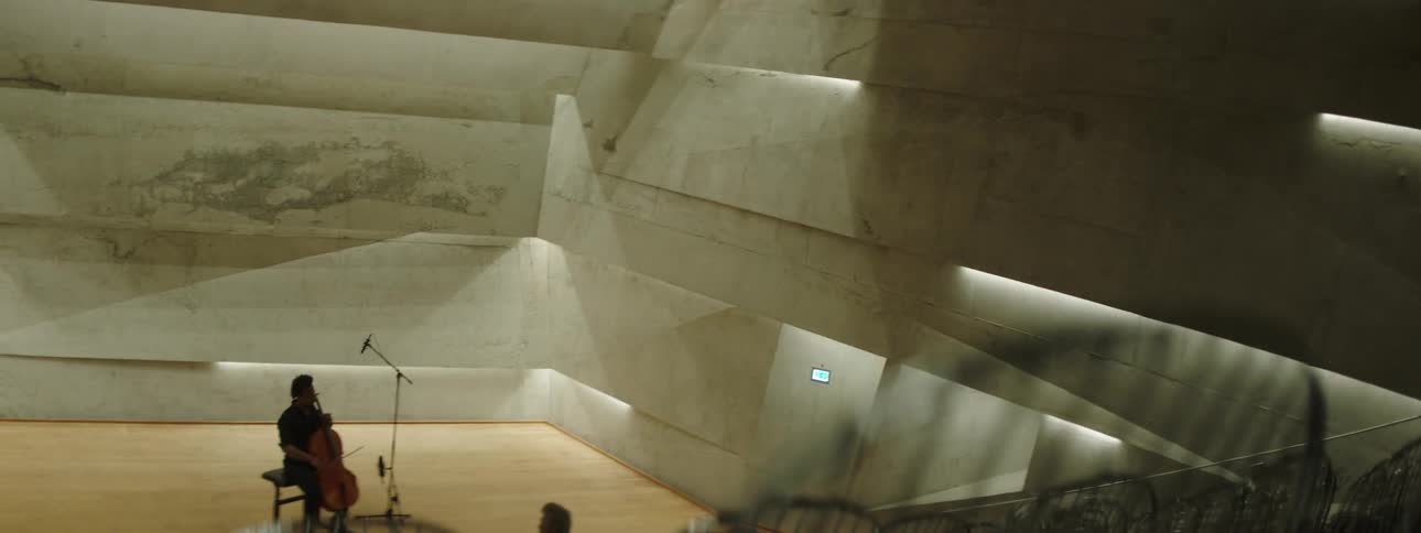 A man playing the cello for a person in the auditorium