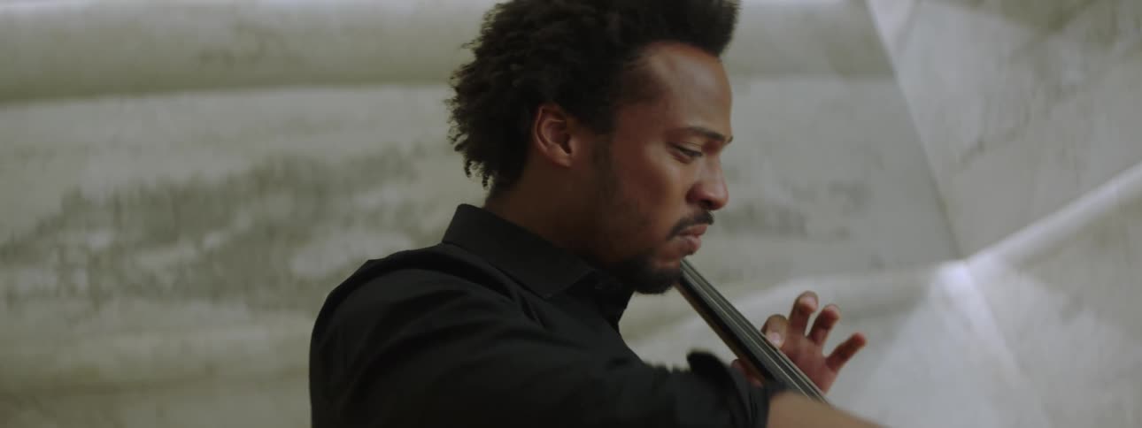 A man musician in black clothing is playing a cello with his hands