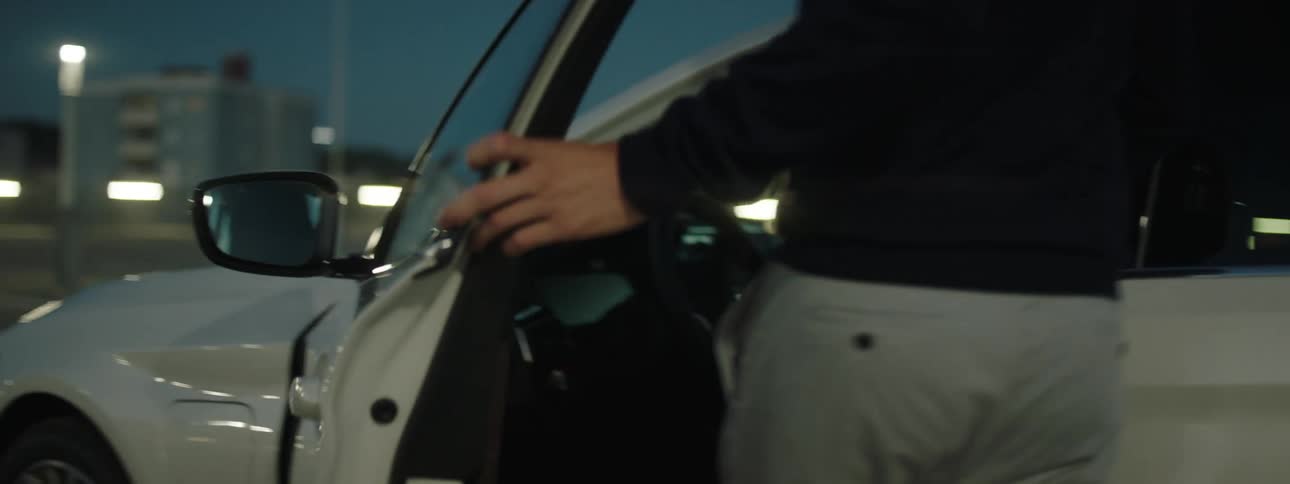 A man in a parking lot walks up to a car opens the door and gets inside