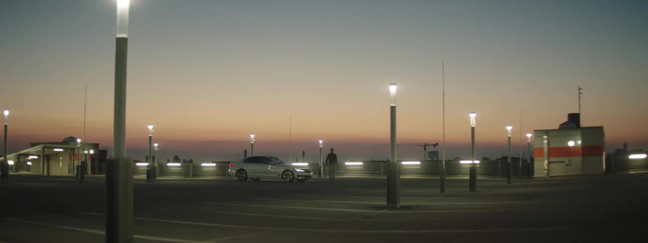A person walking towards a car in a parking lot during sunrise
