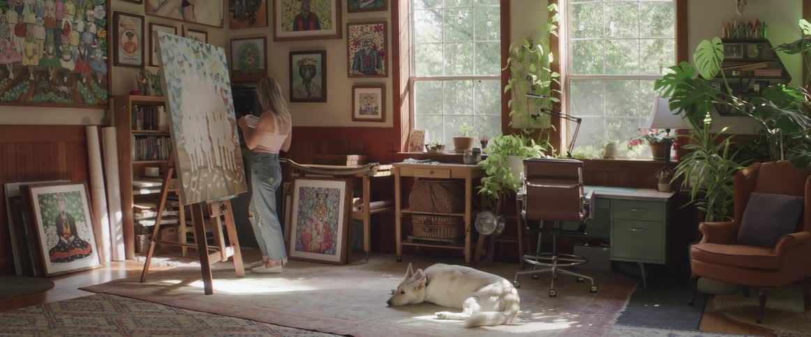 A blonde white woman paints on a large canvas